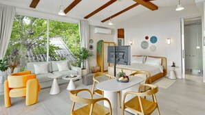 A modern hotel room with a large bed, a dining area, and a sofa. There is a TV, a ceiling fan, and a window with a view of trees. - New Stunning Studio Watching Haad Yao Bay Sunset (Surat Thani)