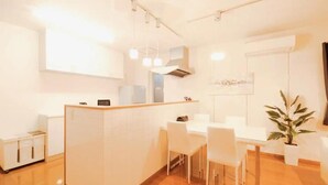A modern kitchen with white cabinets, a dining area with white chairs, and a potted plant. - Familia Design House Sapporo (Sapporo)