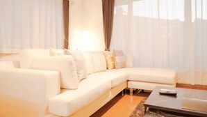 A modern living room with a white sectional sofa, a coffee table, and sheer curtains. - Familia Design House Sapporo (Sapporo)