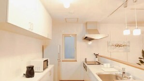 A compact kitchen with white cabinets, a microwave, a sink, and pendant lights. - Familia Design House Sapporo (Sapporo)