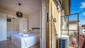 Una camera da letto con un letto, un ampio specchio, un armadio e una porta scorrevole in vetro che dà su un balcone.