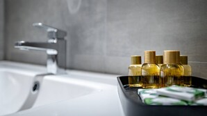 Un bagno con un lavandino bianco, un rubinetto moderno e un vassoio nero con diverse bottiglie di sapone liquido e una saponetta.