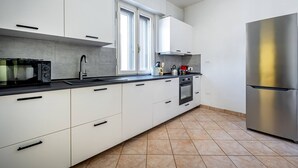 Una cucina moderna con mobili bianchi, un frigorifero in acciaio inossidabile, un forno a microonde e un piano cottura.