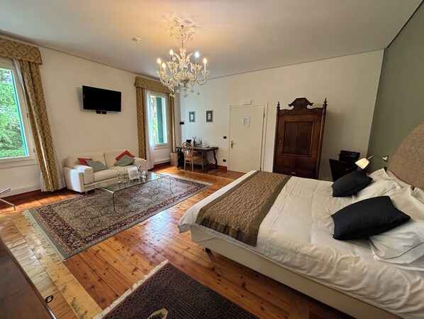 A bedroom with a large bed, a desk, a chair, a television, and a chandelier. - Hotel Villa Ca Damiani (Caneva)