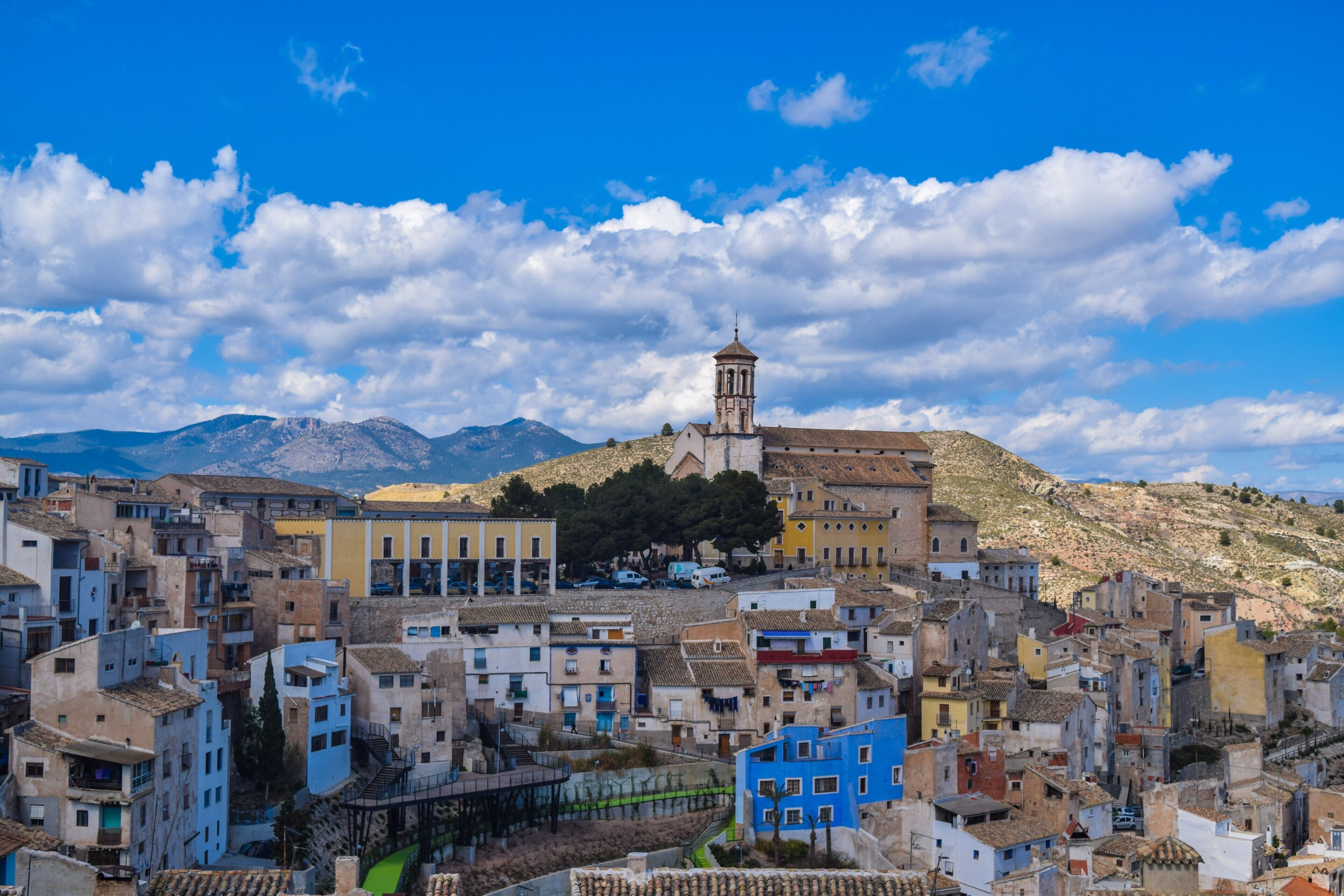 Un pueblo con una iglesia destacada en una colina, edificios apretados y un telón de fondo montañoso.