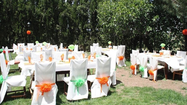 An outdoor event setup with tables and chairs, some with orange and green decorations.