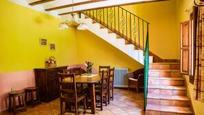 Un comedor con una mesa y sillas de madera, una escalera con barandilla verde, y un radiador en el suelo.