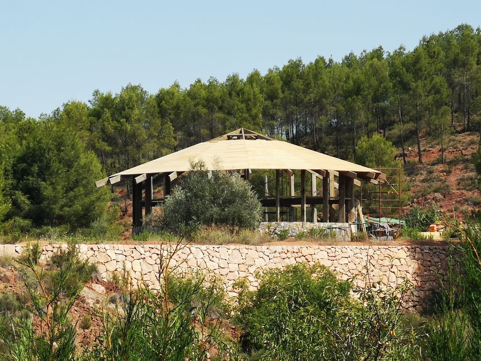 Una estructura de madera con un muro de piedra al frente, rodeada de árboles.