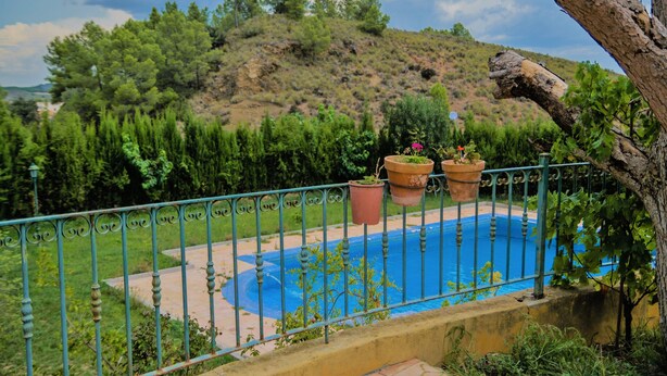 Una piscina con cerramiento de metal, rodeada de vegetación y un paisaje montañoso.