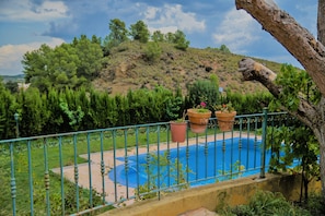Une piscine entourée d’une clôture métallique, bordée de verdure et située dans un paysage vallonné.