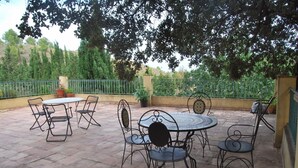 Un patio exterior con una mesa redonda y sillas, rodeado por un muro bajo y una cerca de metal.