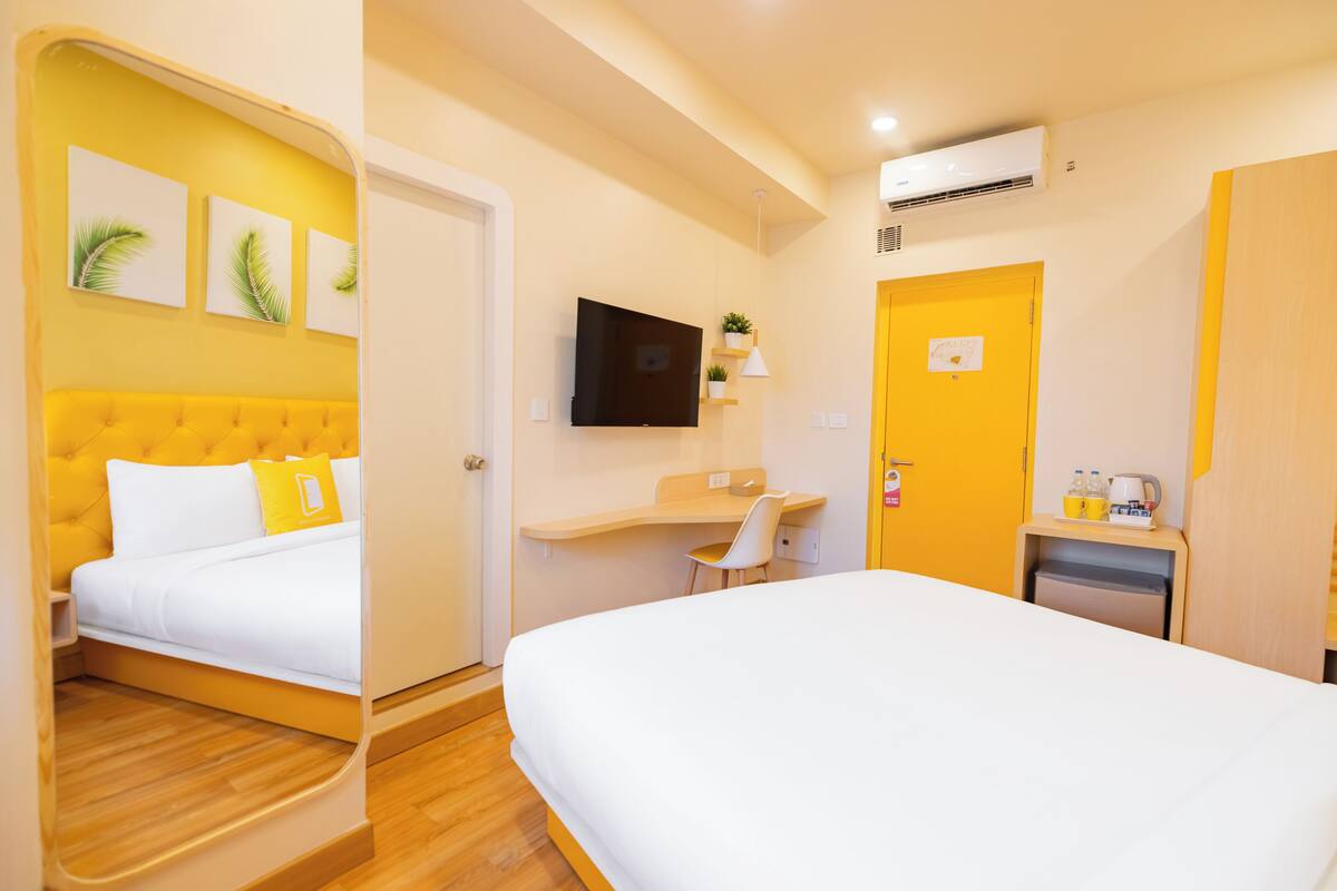 Habitación de hotel con dos camas, un escritorio, televisión y una pequeña cocina.