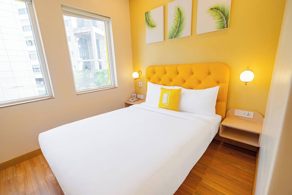 Habitación de hotel con una cama grande, dos mesitas de noche, un ventanal y obras de arte en la pared.