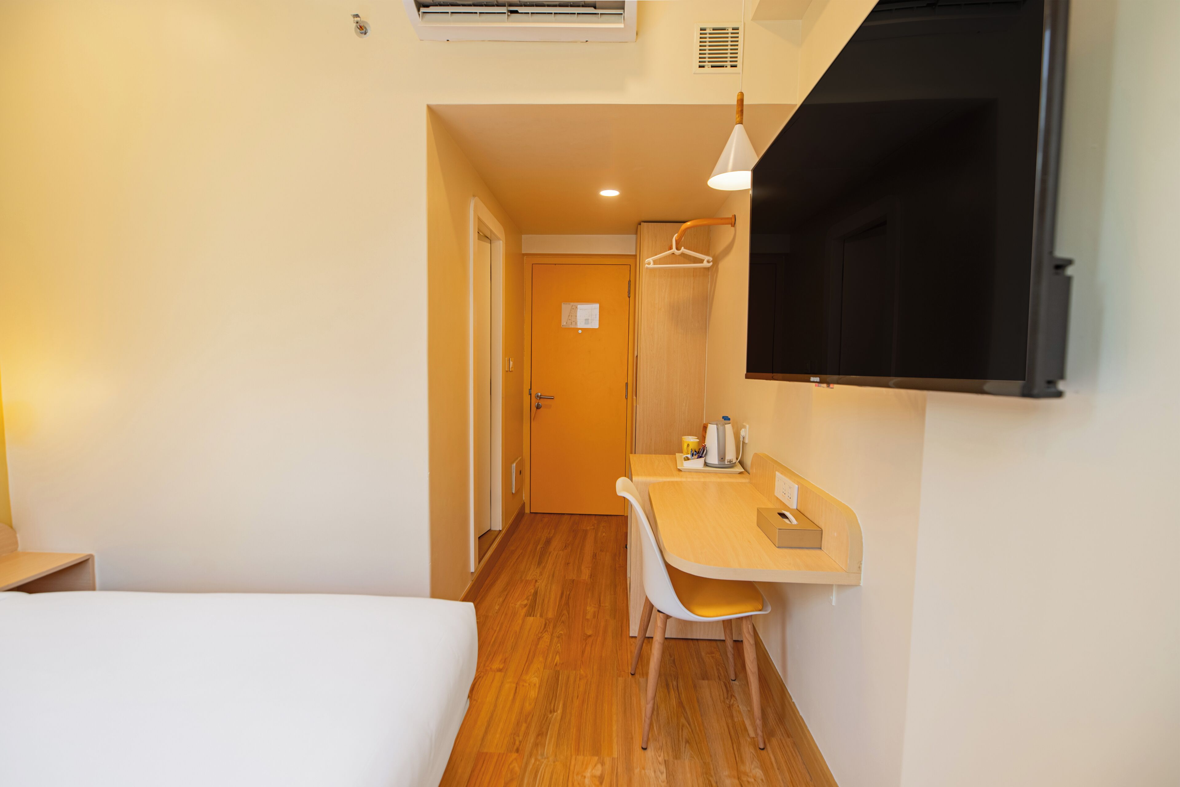 Habitación de hotel con cama, escritorio con silla, televisor montado en la pared y equipo de aire acondicionado.
