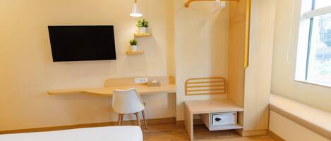 Habitación de hotel moderna con cama, escritorio, silla, televisor montado en la pared, una banqueta pequeña y ventana con vistas.