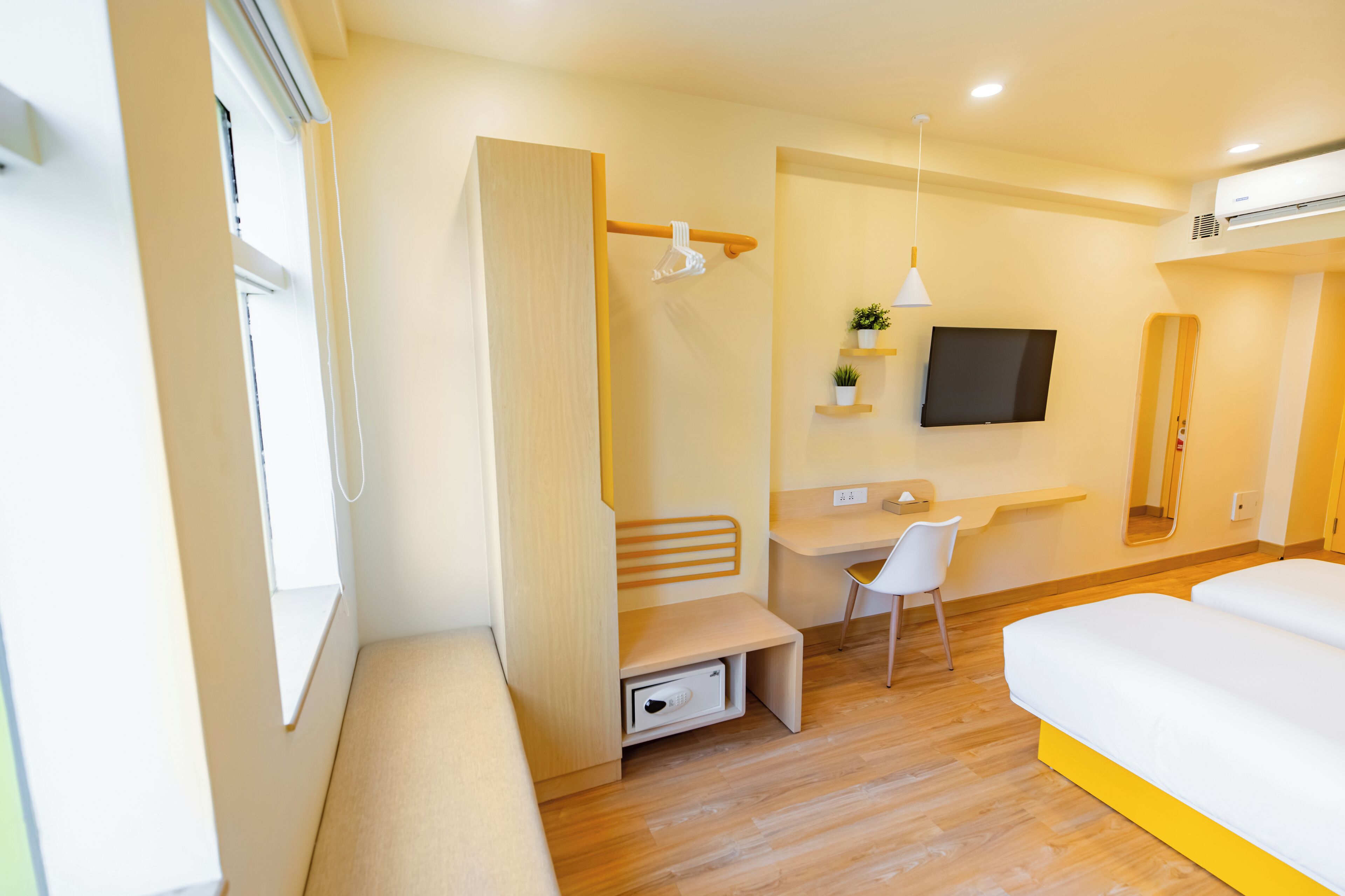 A modern hotel room with a wooden floor, a bed, a desk, a chair, a TV, and a window.