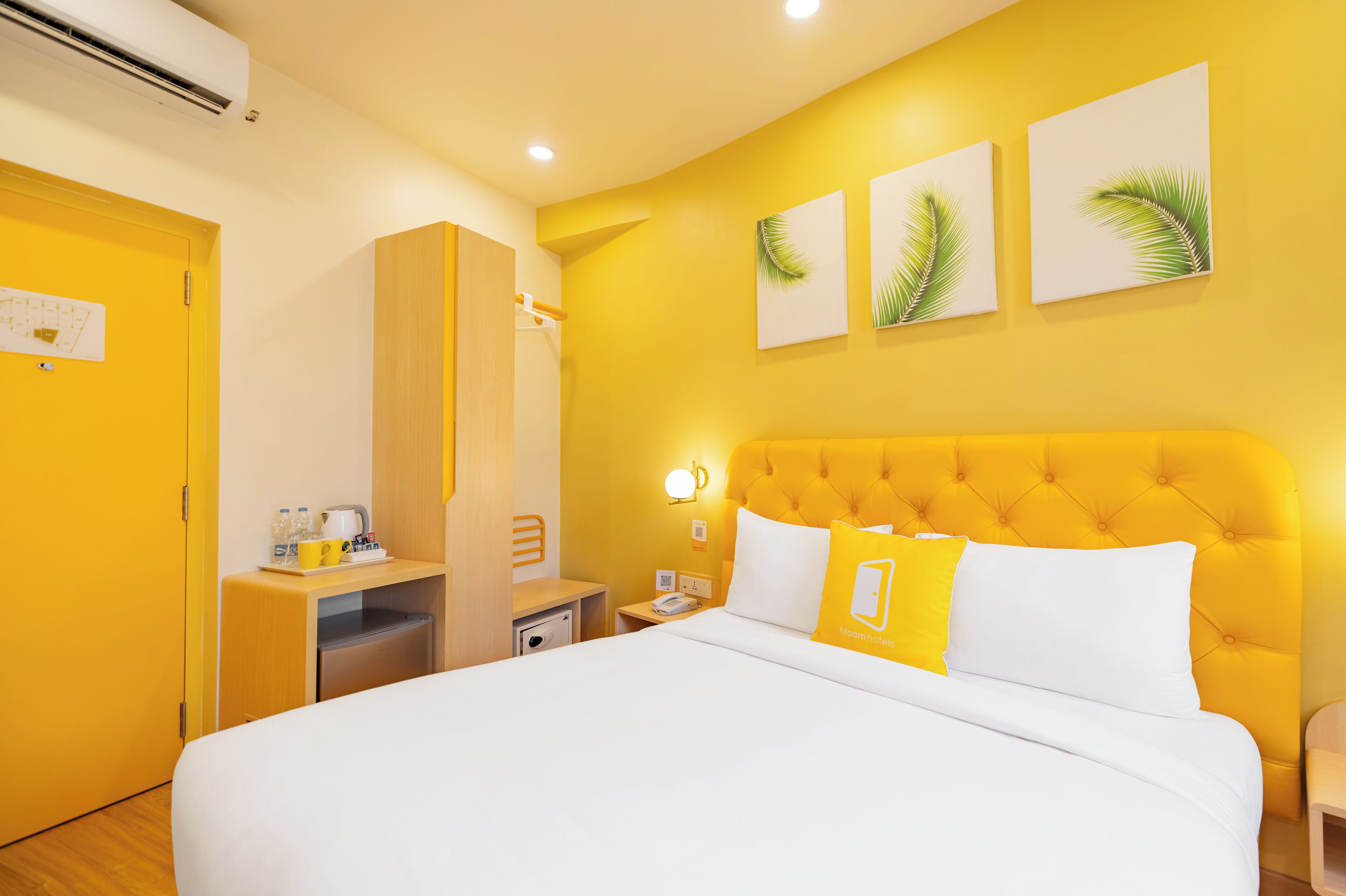 A hotel room with a large bed, a wardrobe, a desk with a lamp, and artwork on the wall.