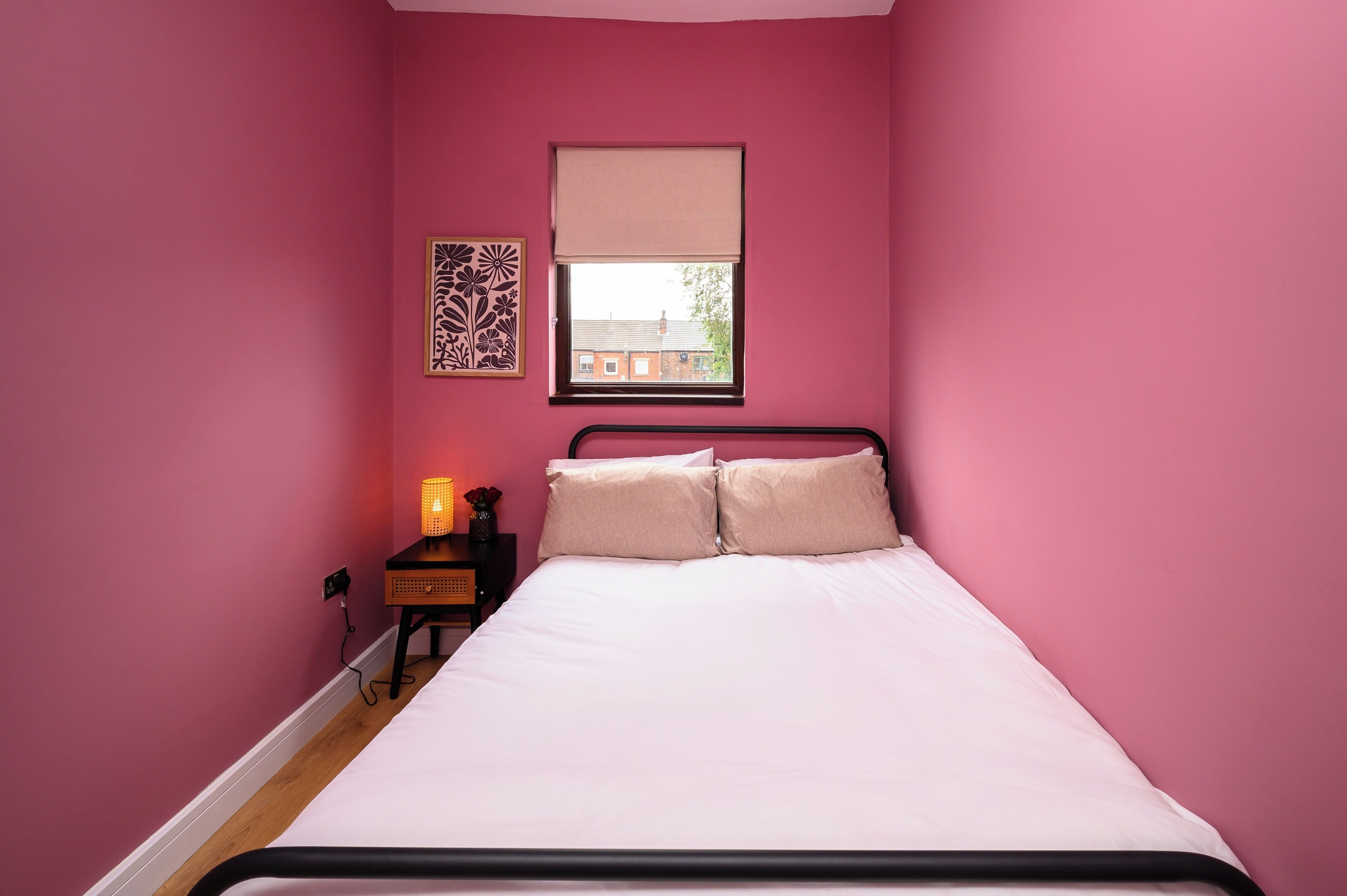 Ein Schlafzimmer mit Bett, Nachttisch, Lampe, Fenster mit Jalousie und Wanddekoration.