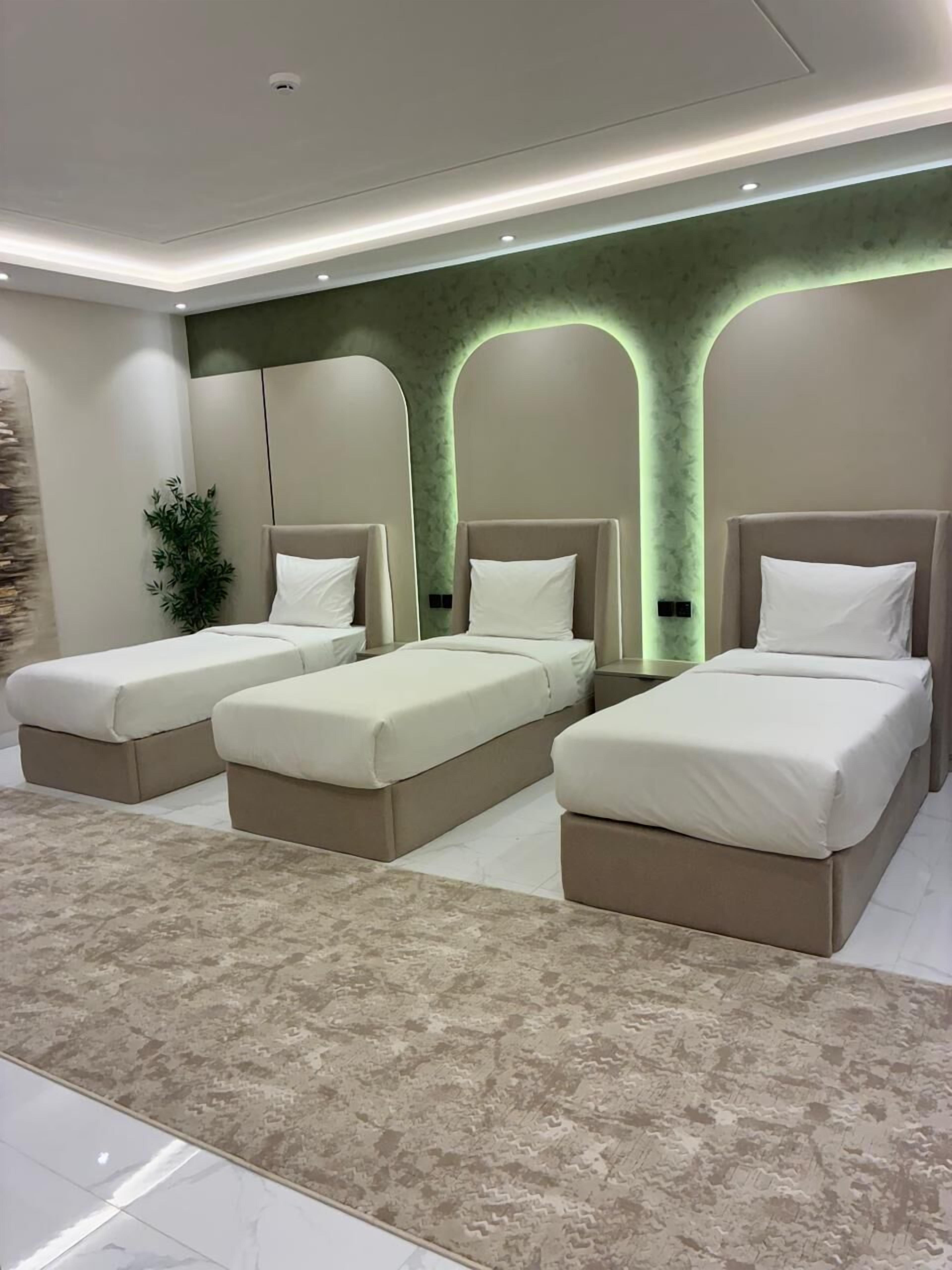 Un dormitorio moderno con tres camas individuales, un ventanal grande y una pared de acento verde.