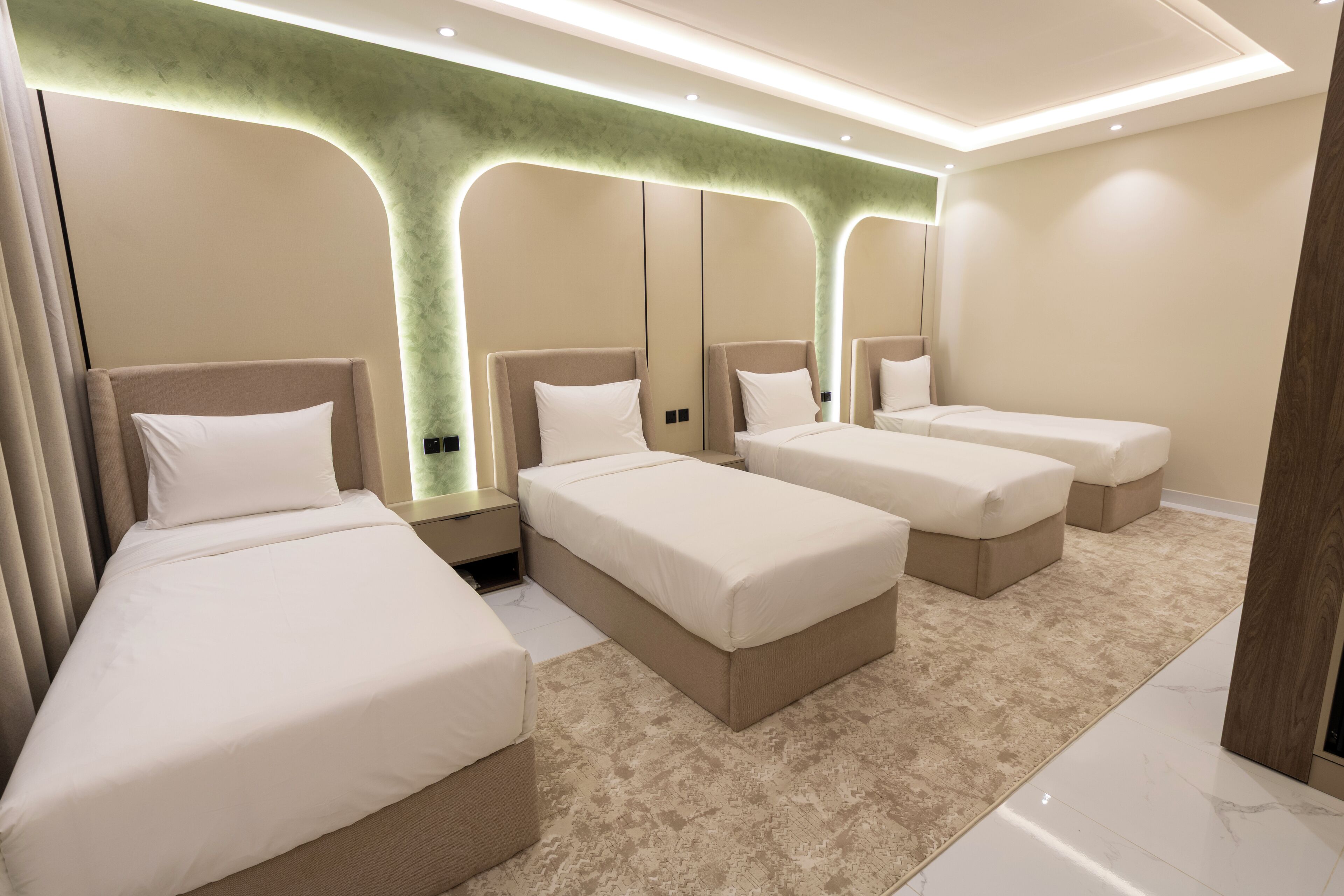 A hotel room with four beds arranged in a row, a green accent wall, and a marble floor.