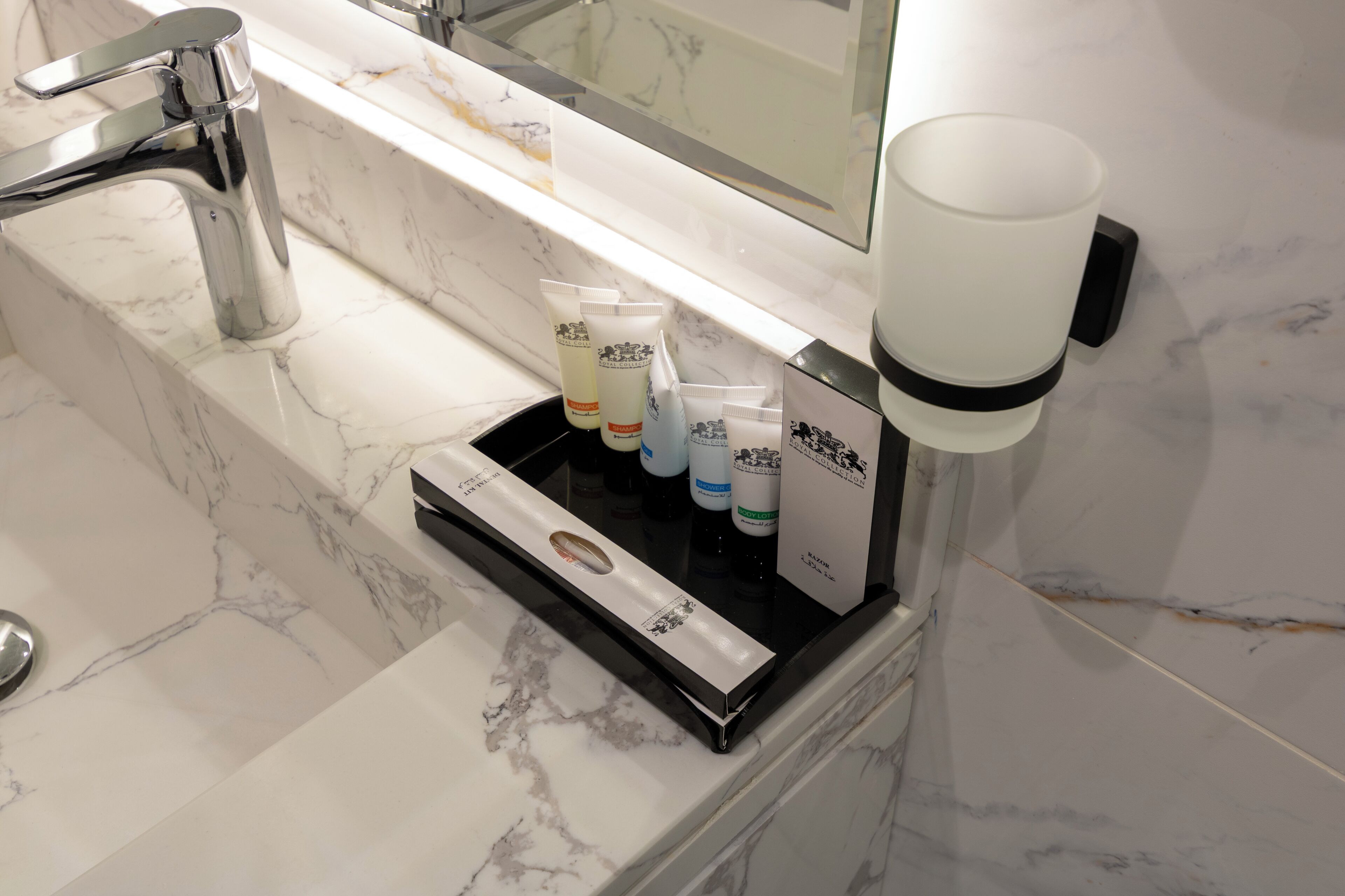 A bathroom with a marble sink, a hand soap dispenser, and toiletries in a tray.