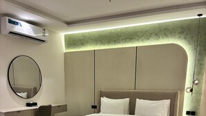 A modern hotel room with a large bed, a round mirror, a desk, a chair, a small round table, and a patterned carpet. - Luxury suites Hotel Apartments (Taif)