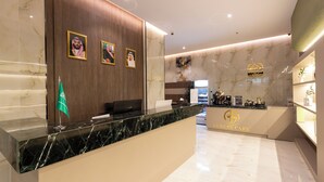 A reception area with a marble counter, framed portraits, a green flag, and a 'Luxury Cafe' sign. - Luxury suites Hotel Apartments (Taif)