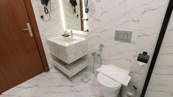 A bathroom with a marble sink, a toilet, a trash can, and a hairdryer mounted on the wall.