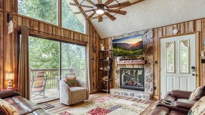 A cozy living room with leather sofas, a fireplace, and a large window overlooking a deck. - Pigeon Forge Mountain View Cabin Rental (Pigeon Forge)