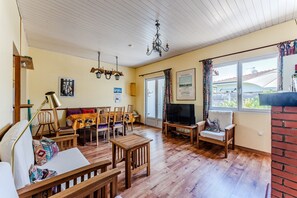 Una sala de estar acogedora con muebles de madera, un televisor y un amplio ventanal con cortinas.