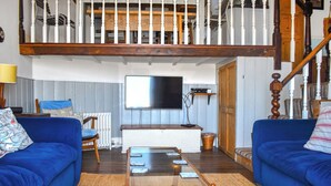 Ein Wohnzimmer mit zwei blauen Sofas, einem Glastisch, einem an der Wand befestigten Fernseher und einer Holztreppe.