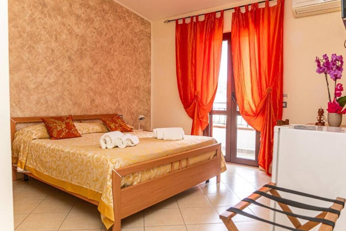 A hotel room with a wooden bed, red curtains, a white desk, and a vase with flowers.