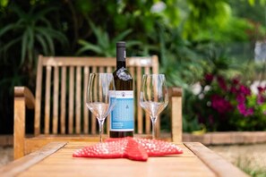 A bottle of wine and two glasses on a wooden table with a garden view in the background. - Cilentiamo (Centola)