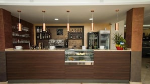 Zona bar moderna con bancone in legno, lampade a sospensione e scaffali con bicchieri e bottiglie.