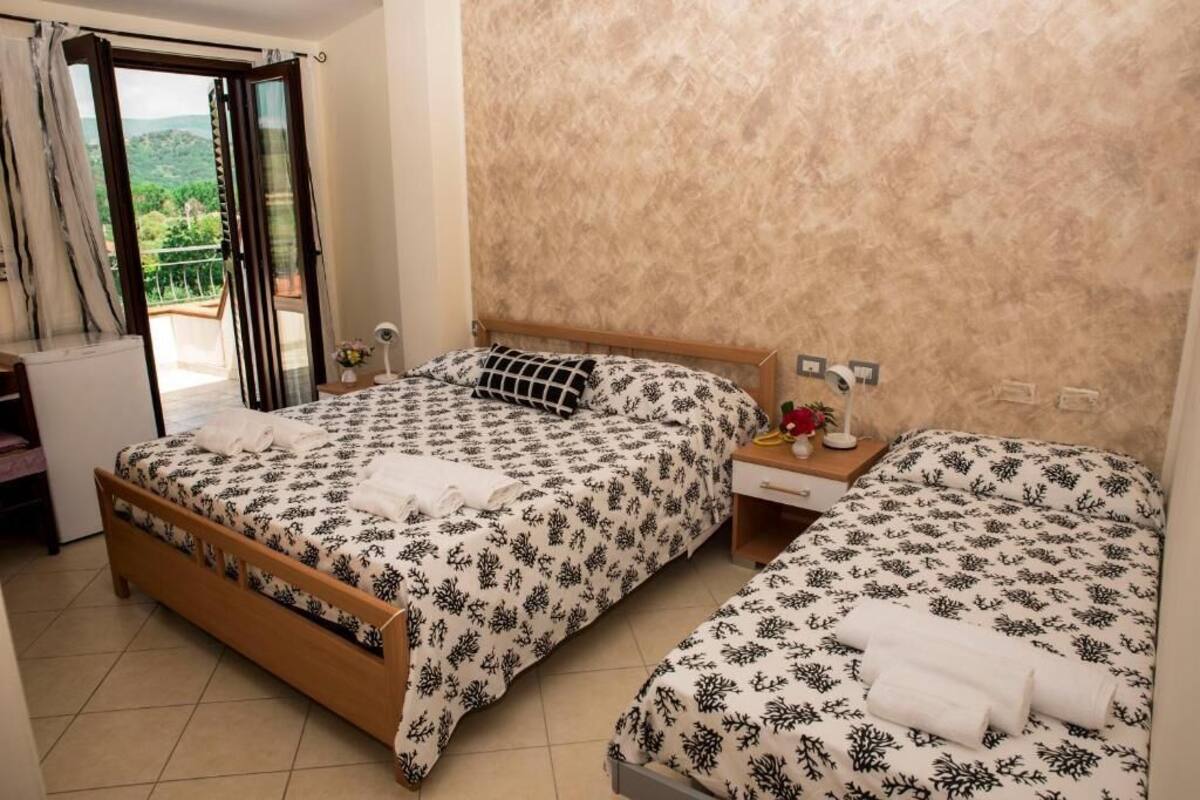 A bedroom with two beds, a wooden headboard, a nightstand, and a view of the outdoors.