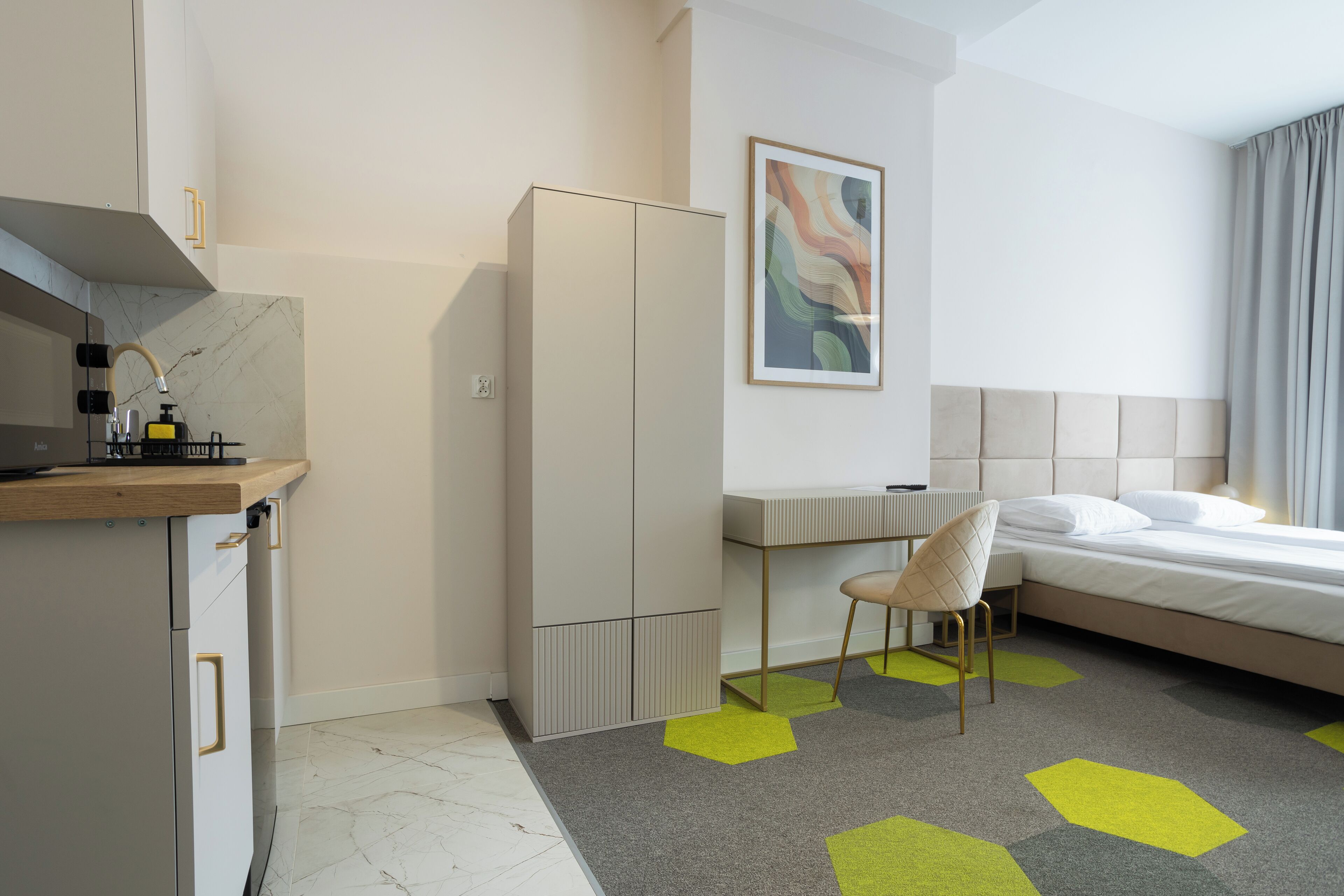 A modern hotel room with a bed, a desk, a chair, and a wardrobe.