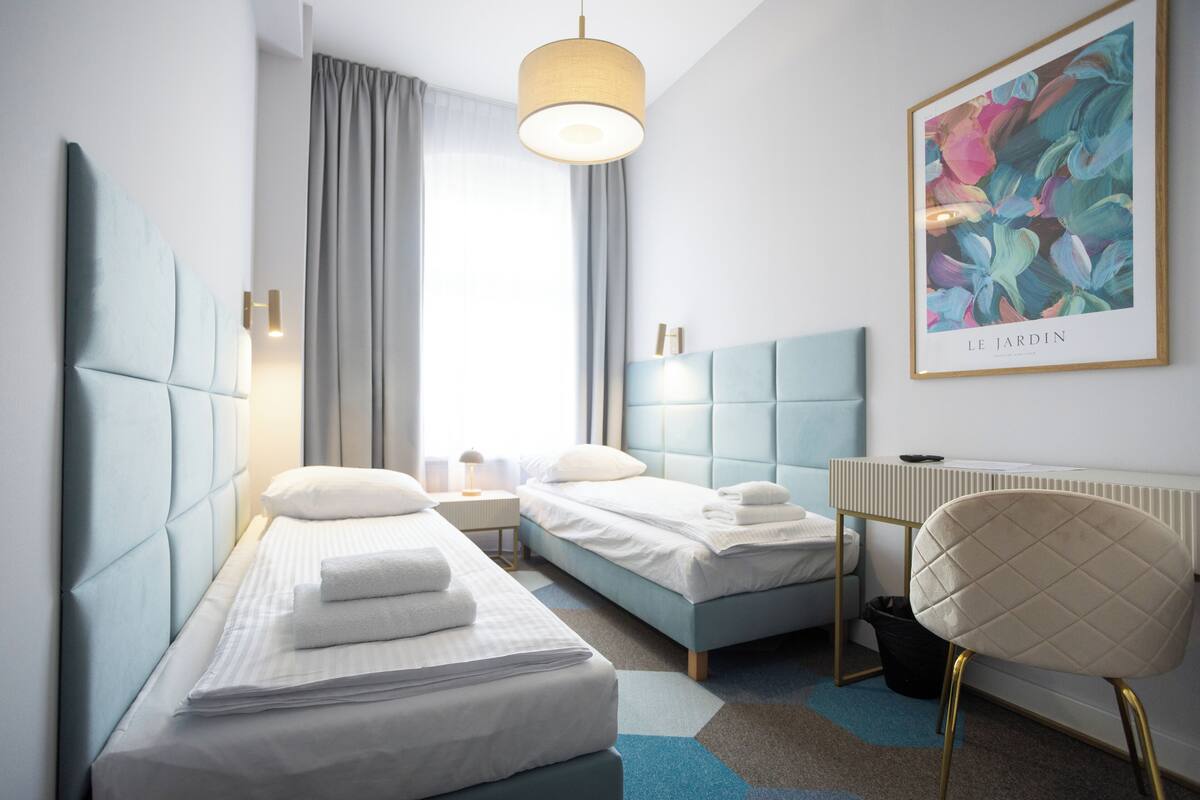 A modern hotel room with two beds, a desk, a chair, and a large window with curtains.