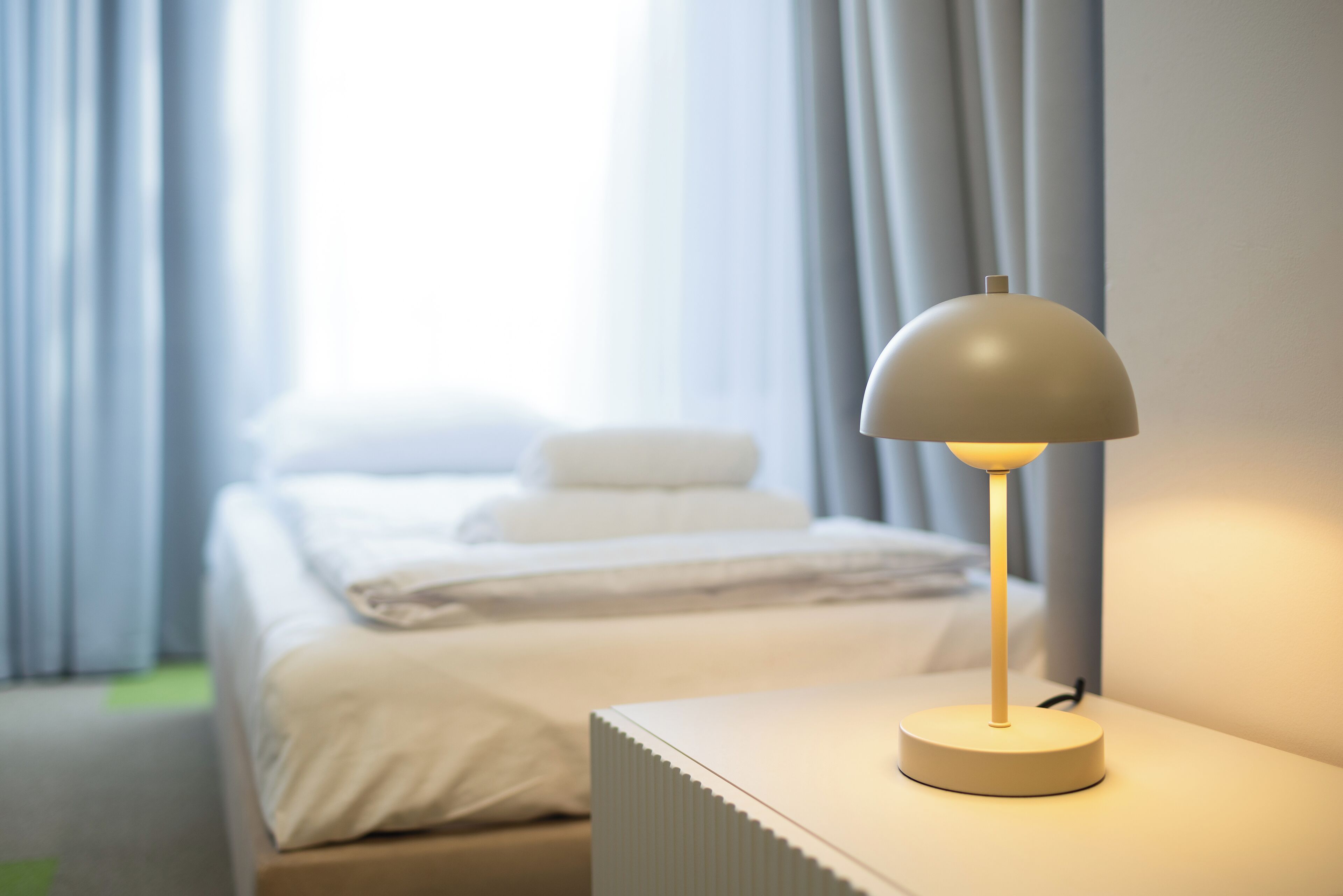 Une chambre d’hôtel avec un lit, une table de chevet avec une lampe et des rideaux.
