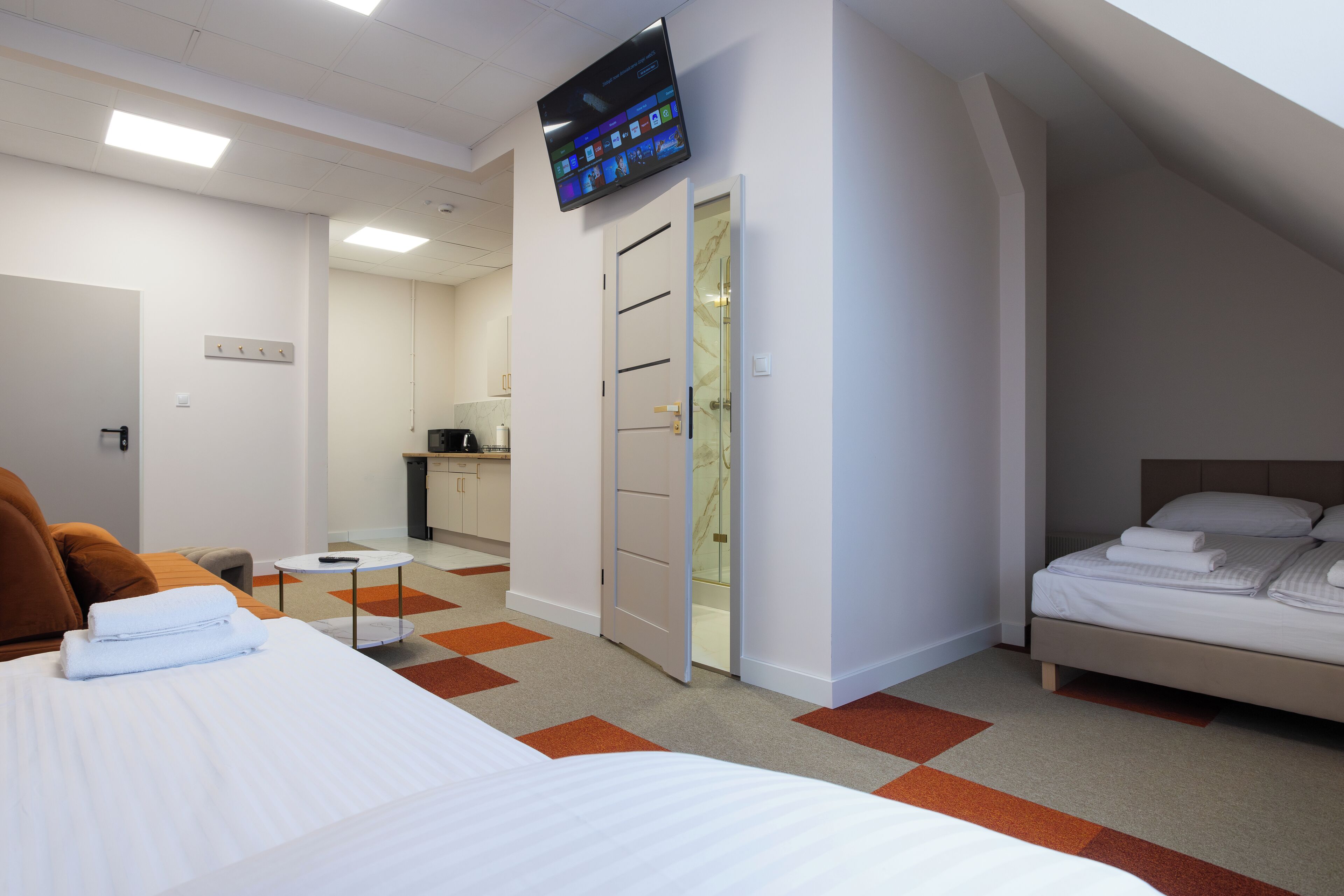 Habitació d'hotel amb llit, televisió penjada a la paret, bany i petita cuina.
