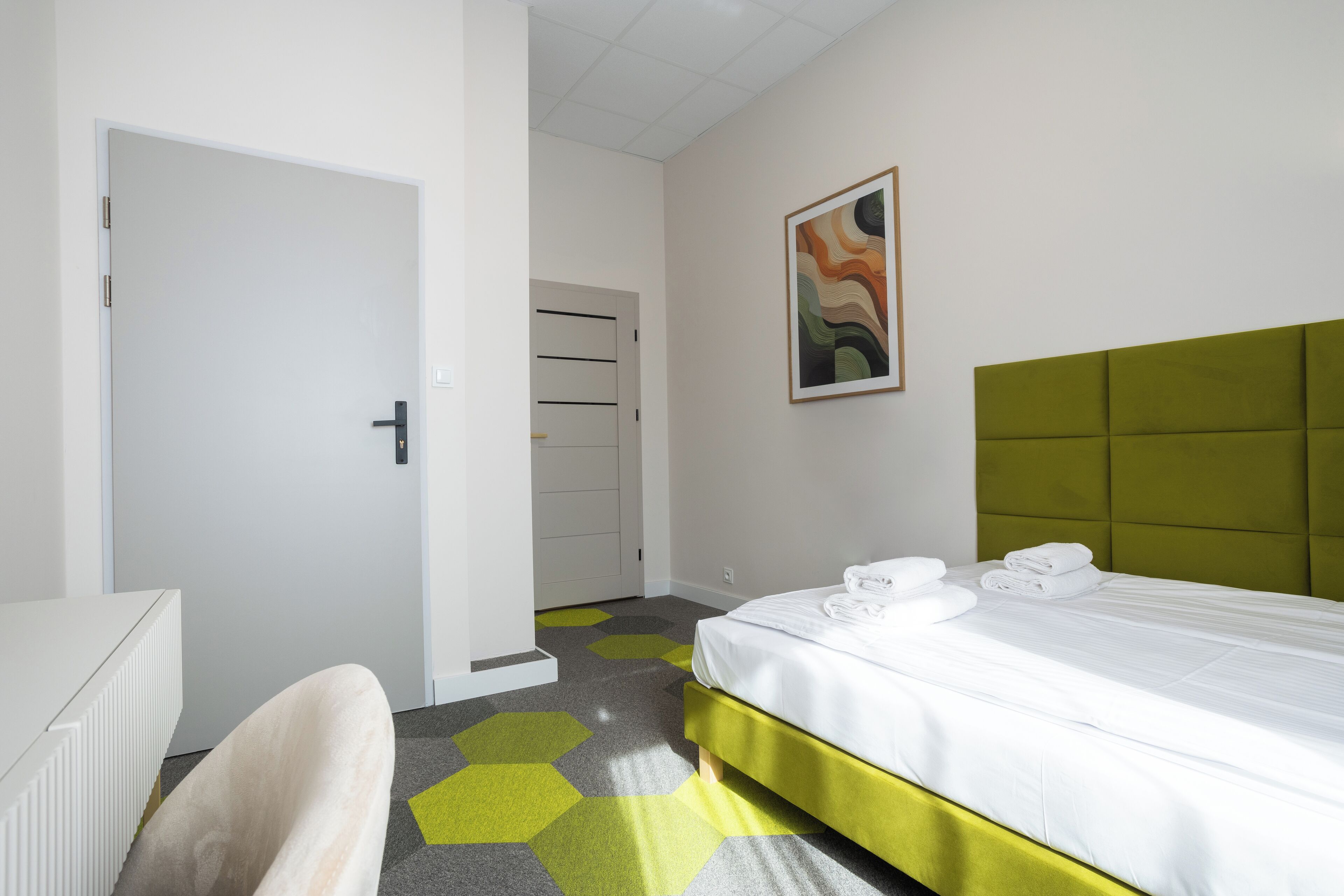 A hotel room with a bed, a chair, a radiator, and a door.
