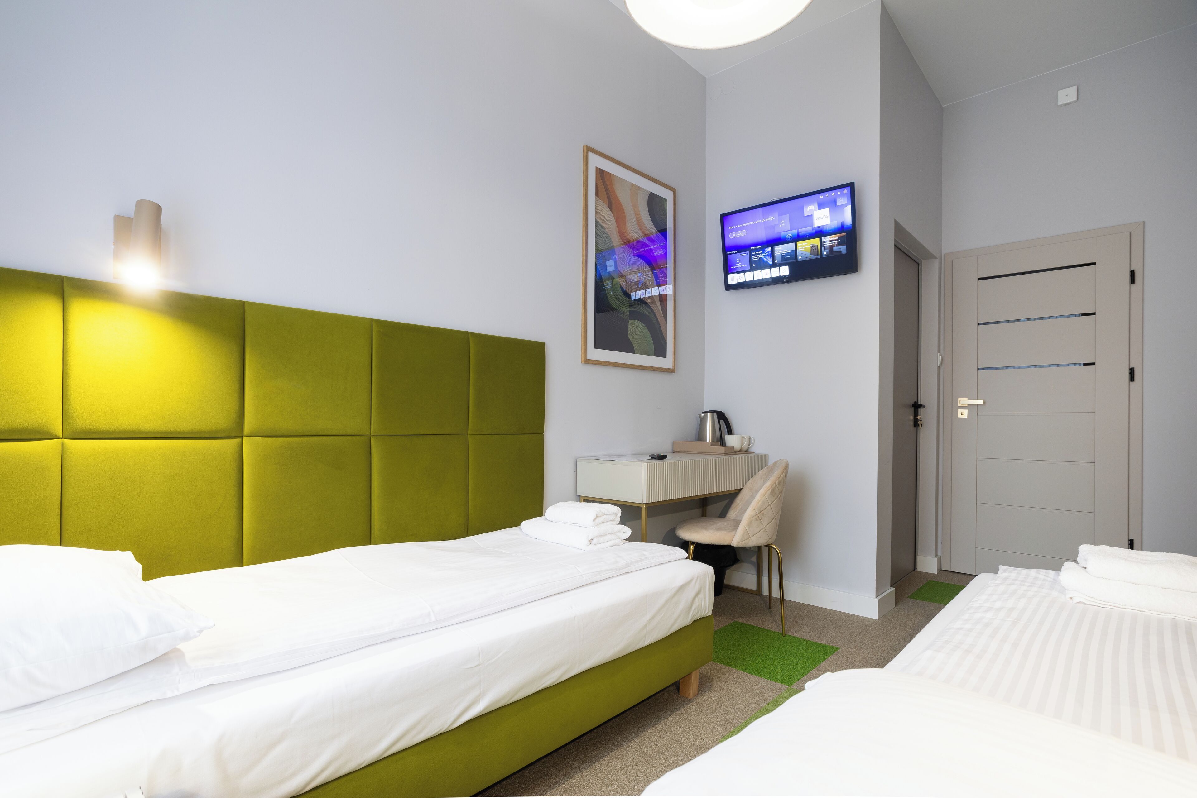 A hotel room with two beds, a desk, a television, and a door.