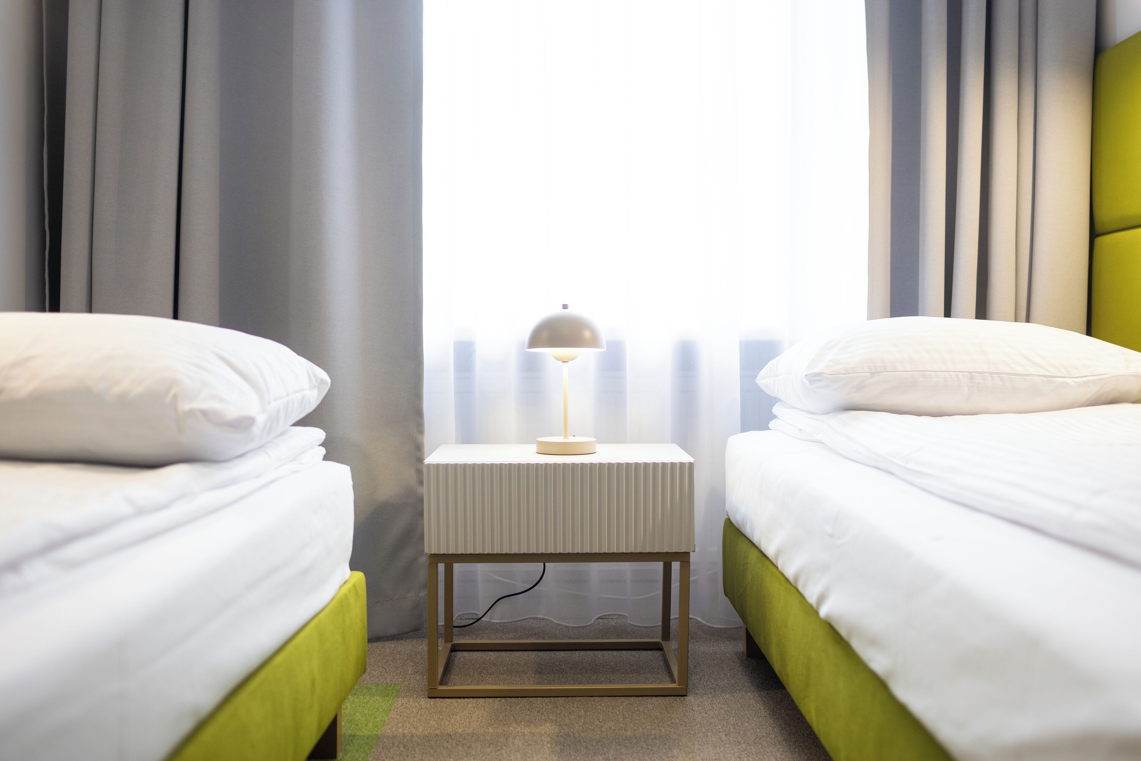 Une chambre d’hôtel avec deux lits, une table de chevet avec une lampe et une vue sur la ville grâce à de grandes fenêtres.