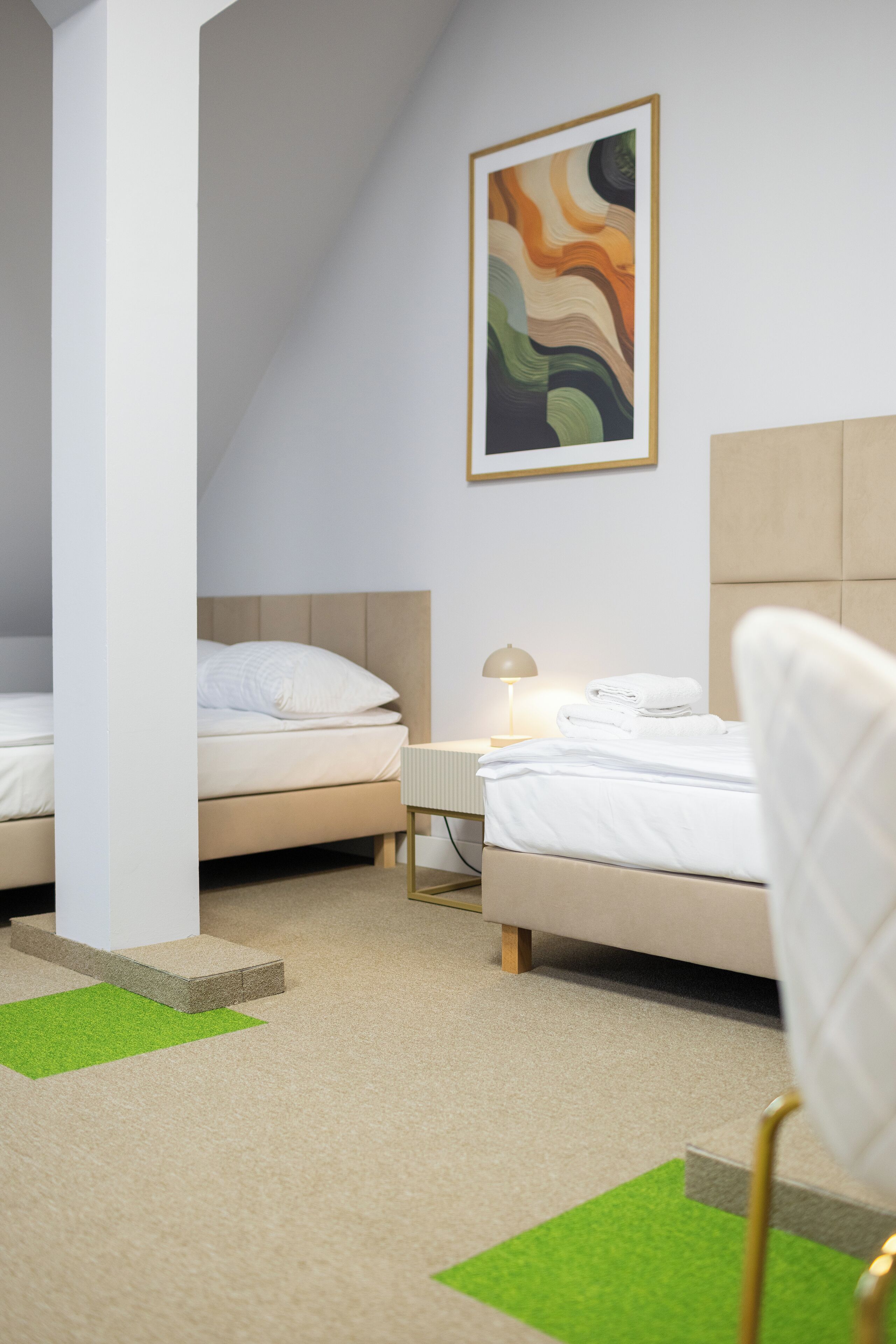 Une chambre avec deux lits, une table de chevet, une lampe et un tapis vert.