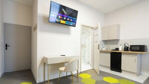 A modern kitchen with a microwave, coffee maker, and a dishwasher. There is a desk with a chair and a flat-screen TV mounted on the wall. - Moon ApartHotel (Wrocław)