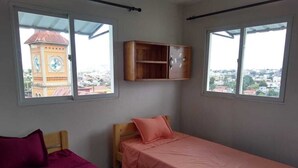 Una habitación con dos camas, un armario de madera y vistas a una torre del reloj a través de una ventana.