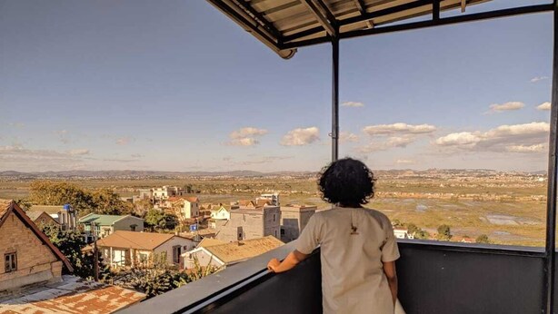 Una persona está de pie en un balcón con vista a una zona residencial con casas y un río.