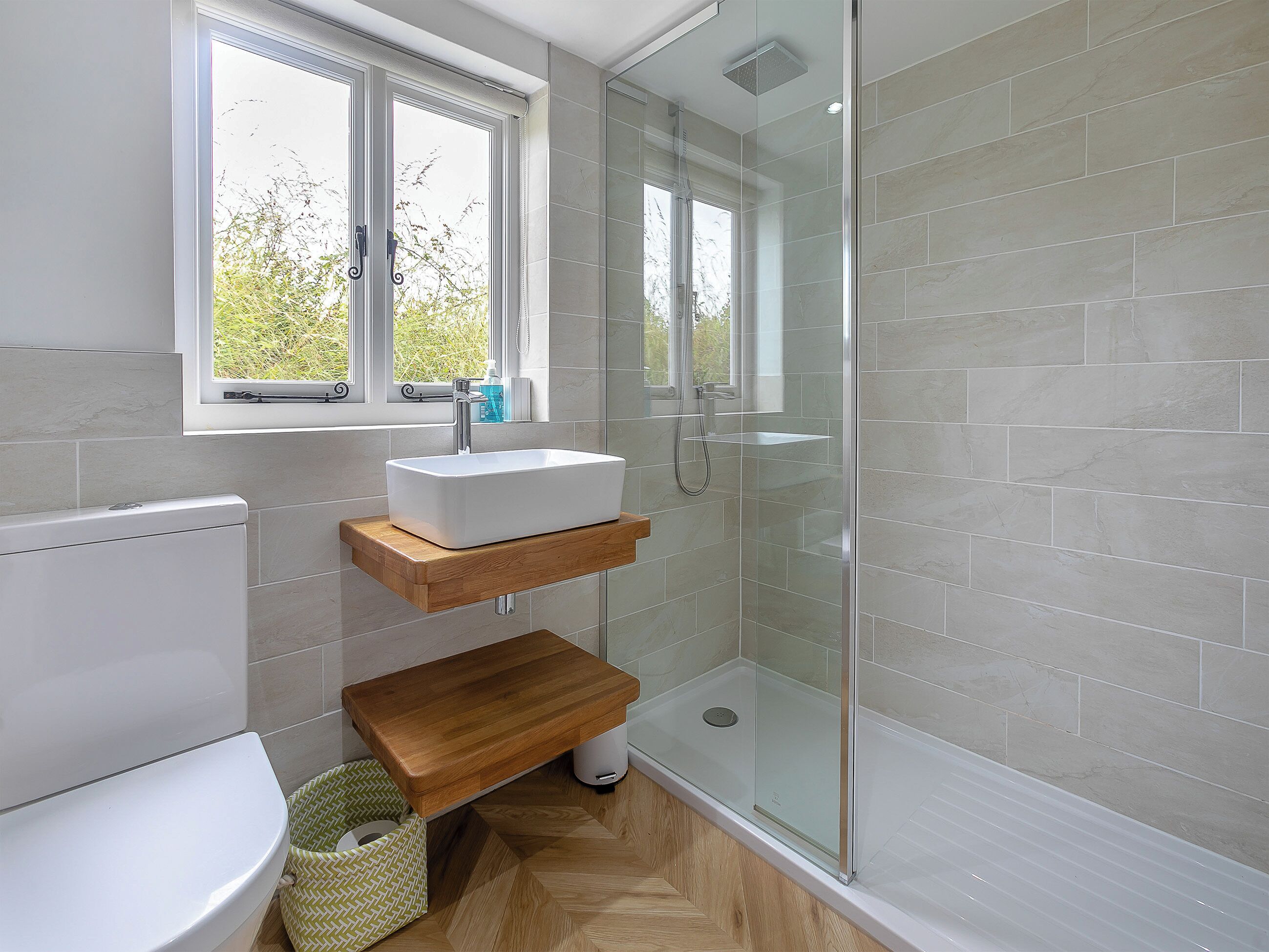 Een moderne badkamer met een douchecabine van glas, een witte wastafel en een houten plank.