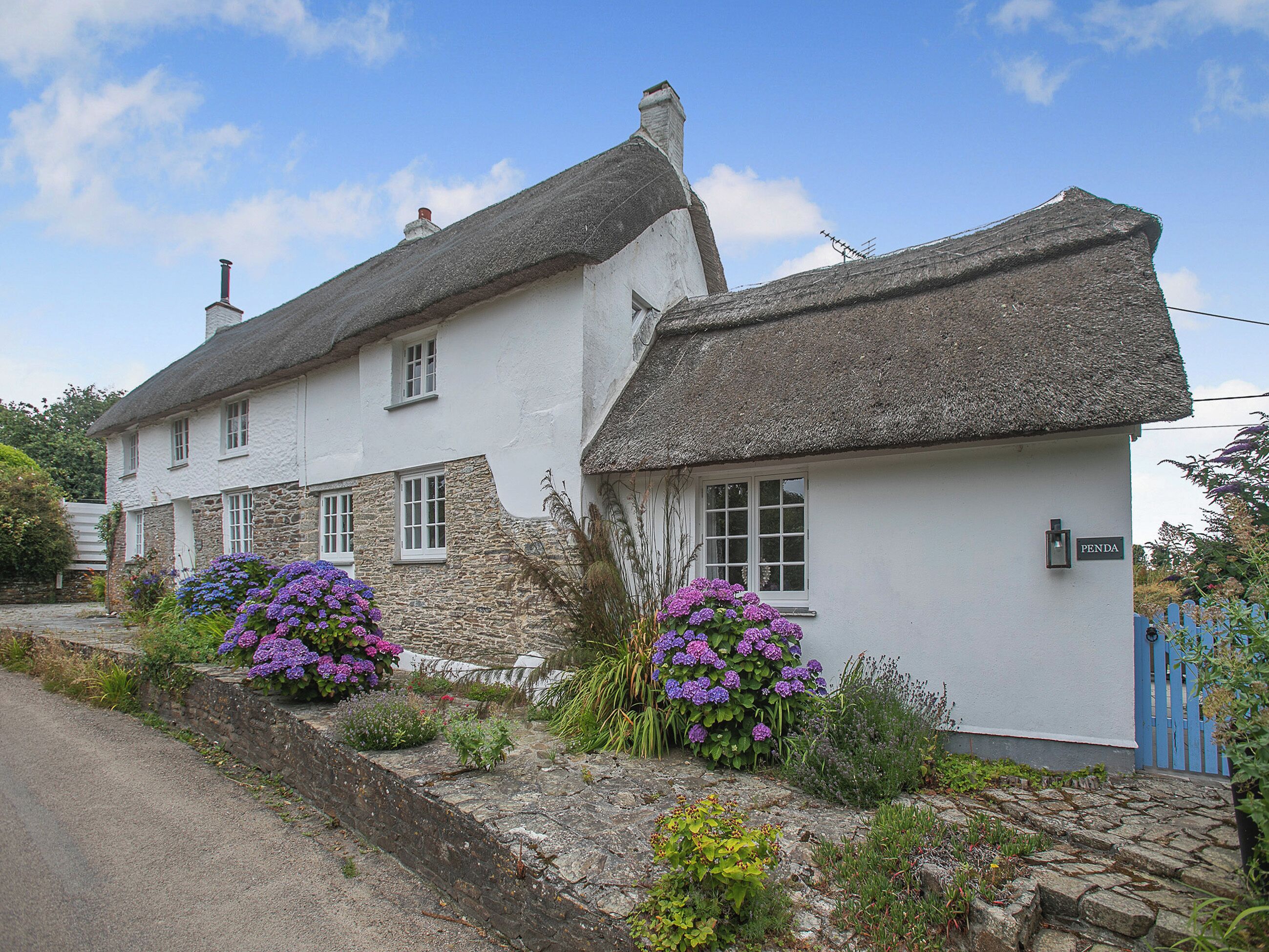 A traditional white building with a thatched roof, stone walls, and a blue gate.