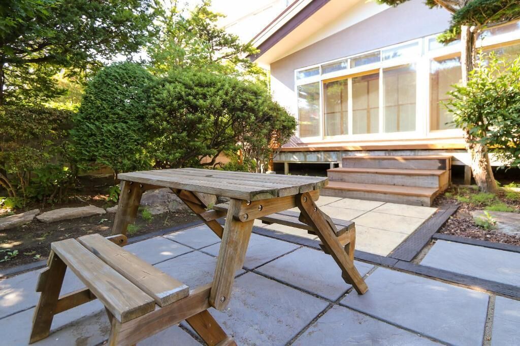 A wooden picnic table with benches in a garden area with a house in the background.