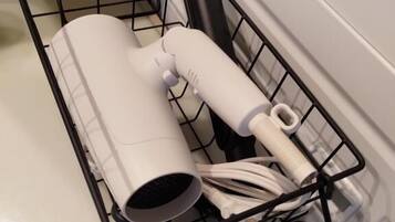 A black wire basket with a white cylindrical object and a white tube, placed on a tiled floor next to a white bathtub.